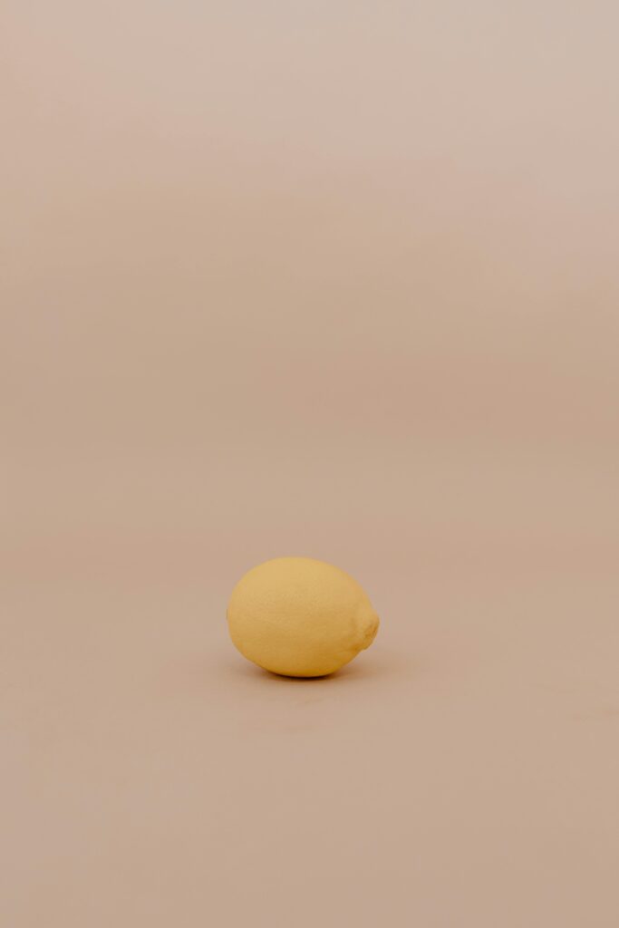 Minimalist photo of a whole lemon on a soft peach background, highlighting simplicity and freshness.